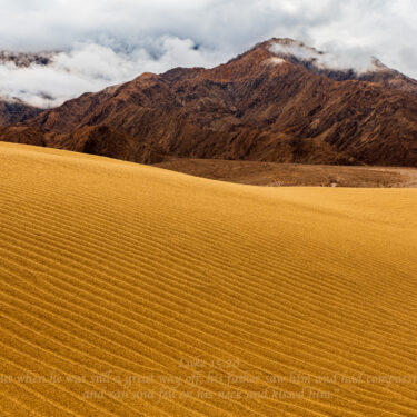 Rippling sand hill joins dark brown rocky mountain.